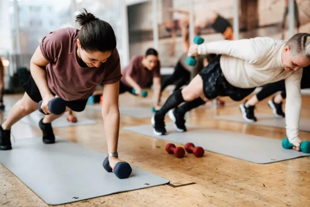 Female friends exercise with dumbbells on mats in a gym class