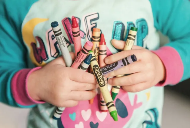 The hands of a child holding many crayons