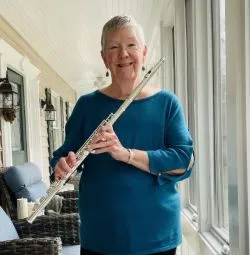 Lyn smiles from a front porch while holding a Haynes flute