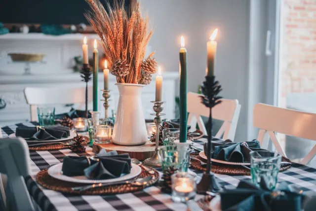 A festive table decorated with a green-checkered table cloth, candles, dinner plates and folded napkins.