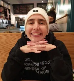 Elena smiles and rests her chin on her folded hands while seated at a restaurant table