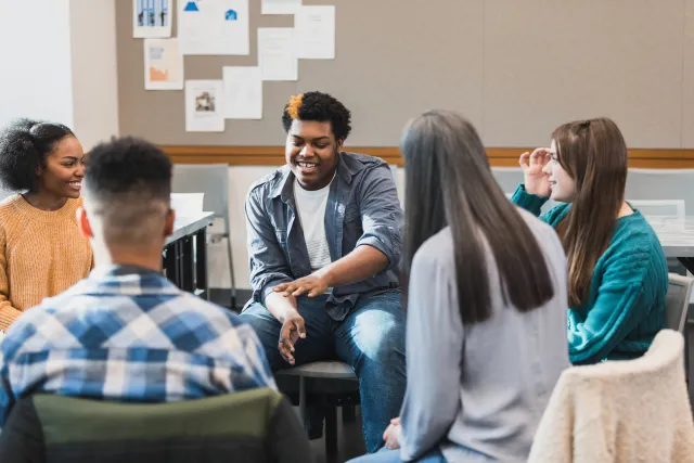 Young adults talk and laugh together while seated around a circle in an indoor group setting