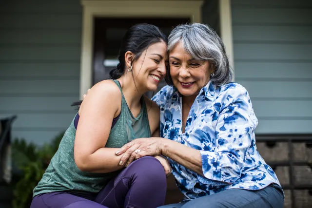 Two smiling women hug side by side on a porch