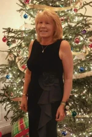 Lisa smiles in an elegant black dress, standing beside a holiday tree