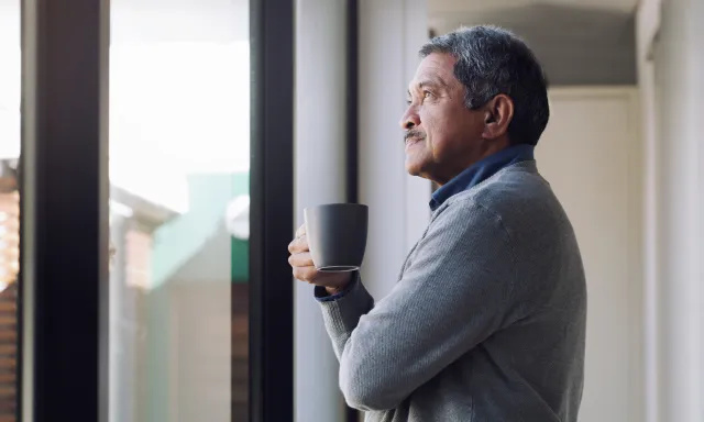Man looking out window with cup in hand
