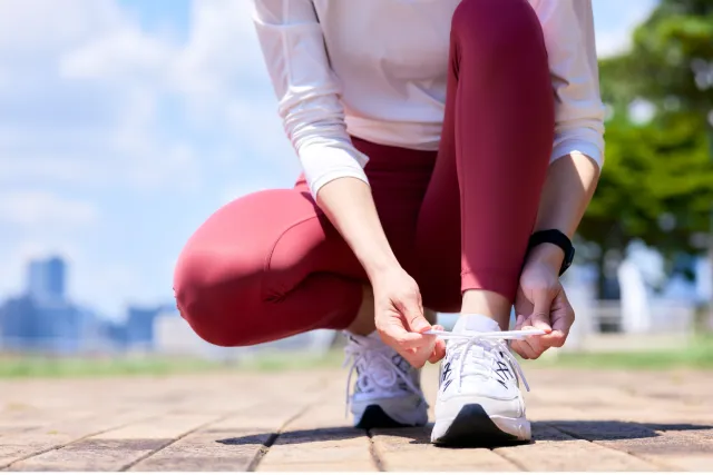 A runner in red athletic leggings ties her sneaker's laces