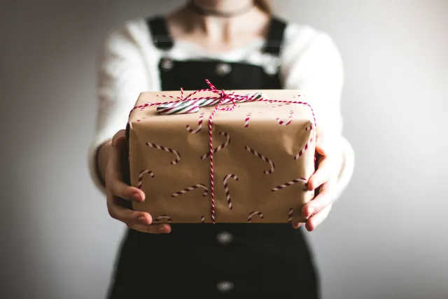 An unseen person presents a gift box wrapped in candy-cane gift paper