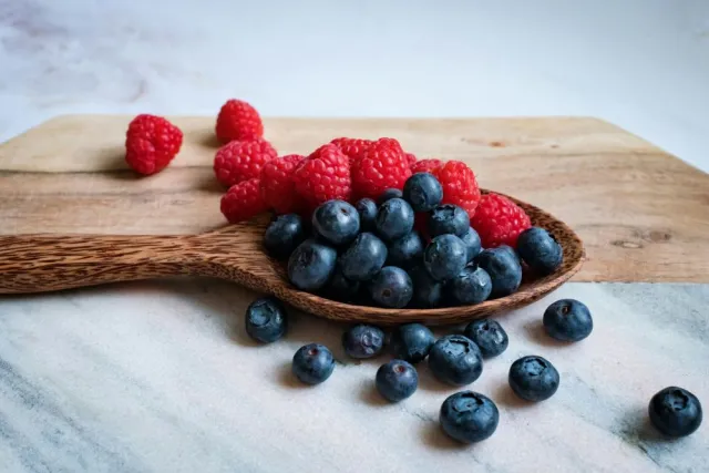 A wooden spoon full of blueberries and raspberries