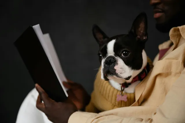 A man sitting with an open book and pet dog in his lap