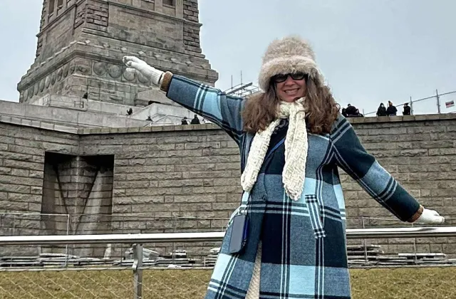 Olga pictured in winter coat and hat stands near the Statue of Liberty  
