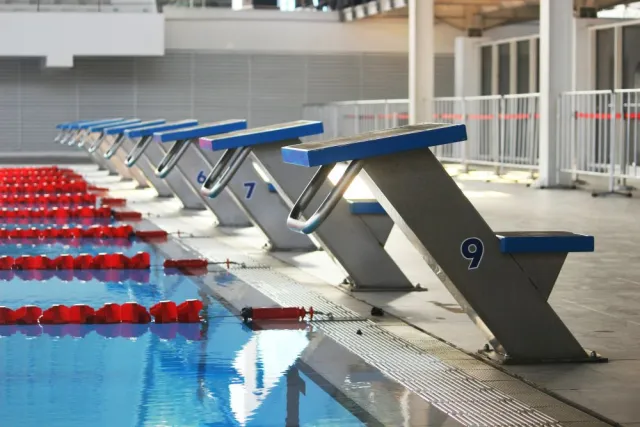 A row of blue starting blocks line the edge of an empty swimming pool