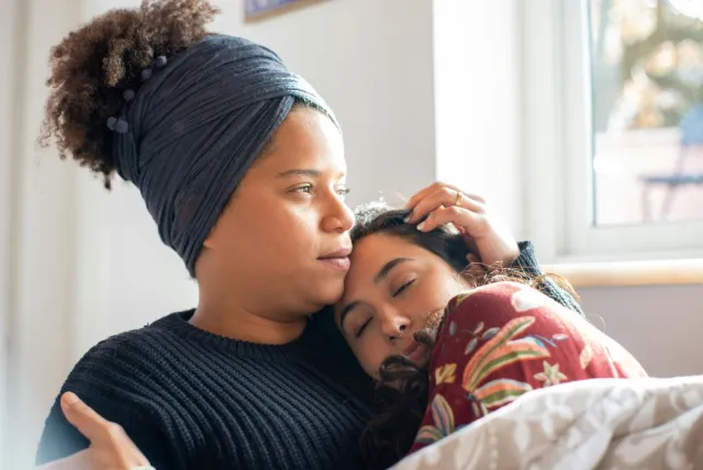 Two women hold each other while seated in a living room