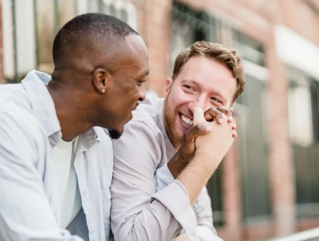Two men sit together on a city apartment step holding hands