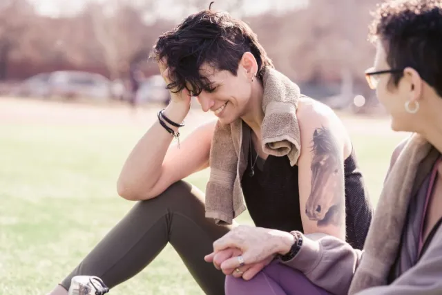 Two women laugh and hold hands in a park