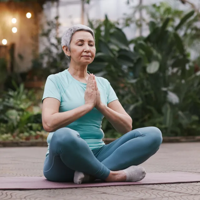 A woman with short gray hair practices meditation while seated on yoga mat