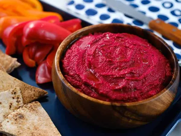 creamy beet hummus in a wooden bowl with peppers and pitas