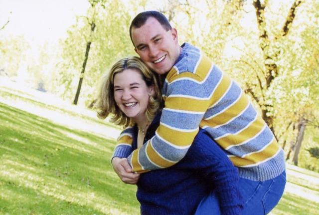 Kelly and Justin smile while Kelly carries Justin piggyback in a sunlit park