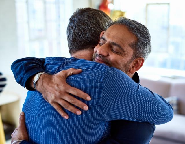 Two men wearing blue dress shirts hug each other supportively