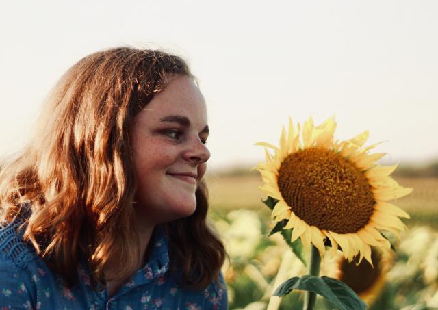 A young woman smiles while looking at a large sunflower