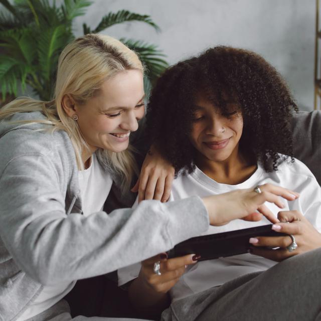 Two friends sit beside one another looking at a digital tablet