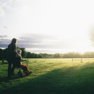 female pushing older person in wheelchair in field