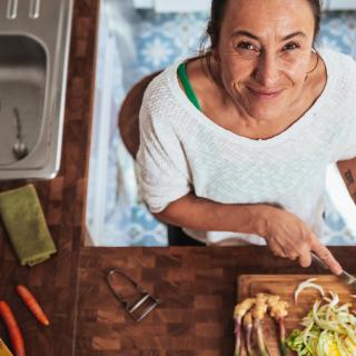 A woman smiles while chopping vegetables on a cutting board in her kitchen