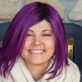 Amber smiles from inside her home with bright purple hair.