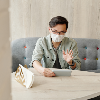 A young man wearing a mask speaks to someone on his mobile phone while sitting at home