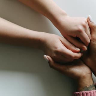 A woman's hands comfortingly hold the hands of a friend