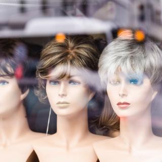 A store window features women mannequin heads with different wig styles