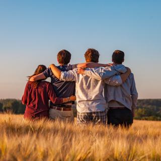 Friends stand side by side with their arms around one another, looking out at a blue sky