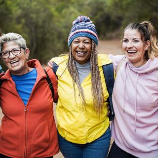 A diverse group of women smiling in jackets outdoors with their arms around one another