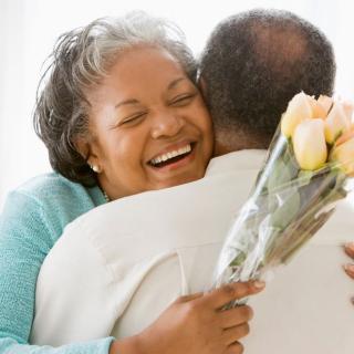A woman smiles and hugs a man as she holds a bouquet of roses
