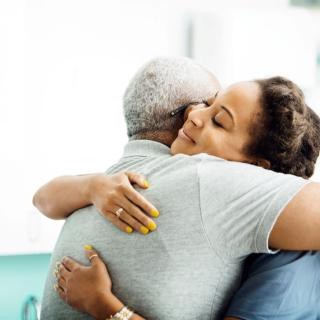 A side view of a female doctor hugging an older man in a clinic