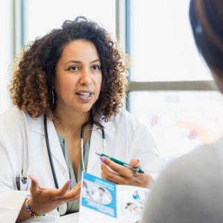 A female doctor talks with an unseen young woman holding a patient information brochure
