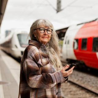 A mature woman with long hair and dark glasses waits at a train station