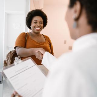 A woman arriving at a medical office smiles and shakes hands with a female doctor