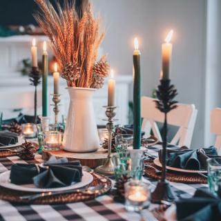 A festive table decorated with a green-checkered table cloth, candles, dinner plates and folded napkins.