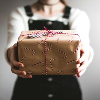An unseen person presents a gift box wrapped in candy-cane gift paper