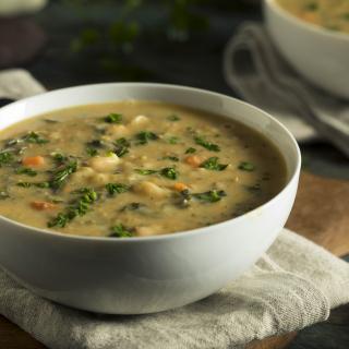 A ceramic bowl filled with a soup containing greens and white beans