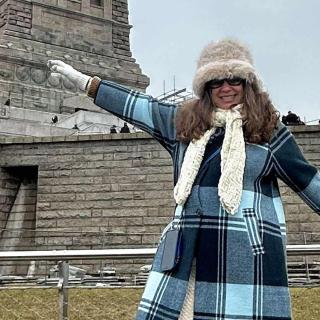 Olga pictured in winter coat and hat stands near the Statue of Liberty  