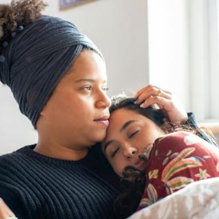 Two women hold each other while seated in a living room