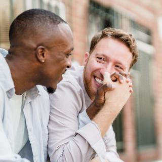 Two men sit together on a city apartment step holding hands