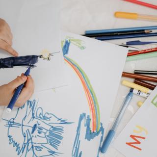 Child's small hands hold a marker while creating a colorful drawing