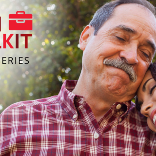 A daughter smiles and rests her head on her father's shoulder in front of a tree
