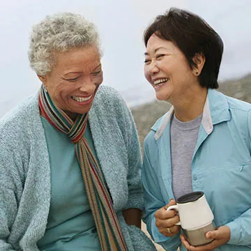 two women of different races smiling and laughing on a walk