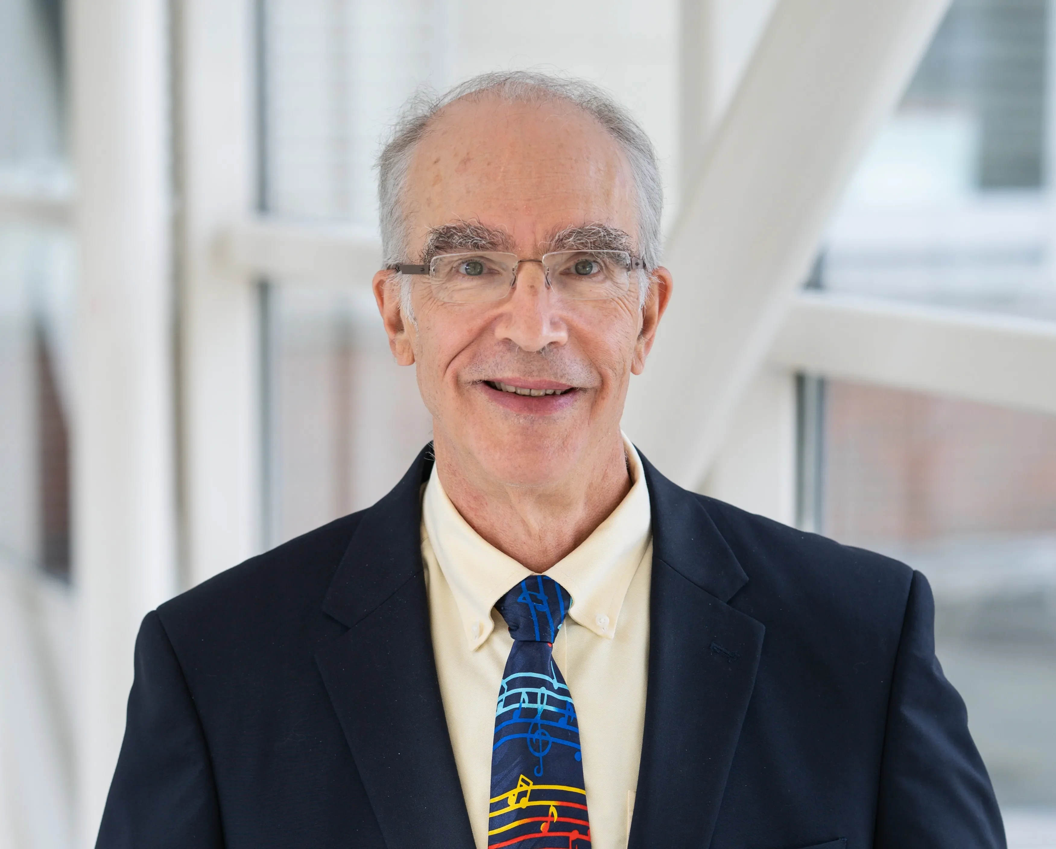 Dr. Stephen Edge wears a suit and tie and smiles beside a window within a modern building