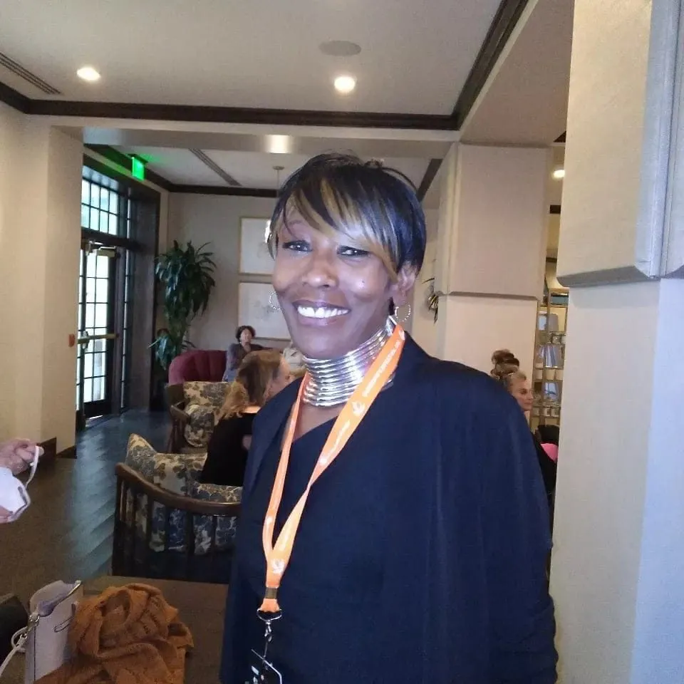 Denyse smiles in a black dress and gold necklace 