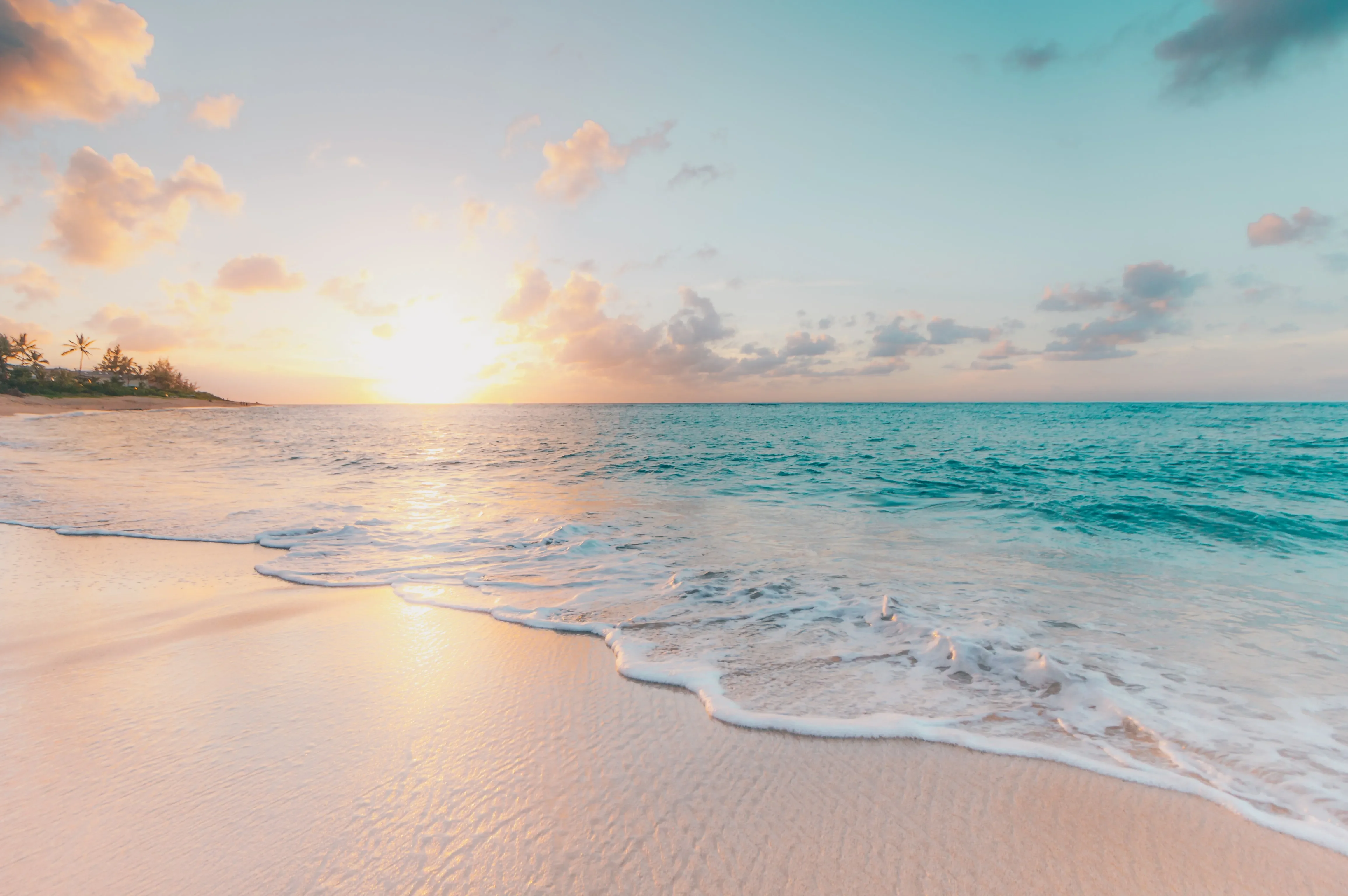 A sandy beach is lit by the sun as it shines over an ocean horizon