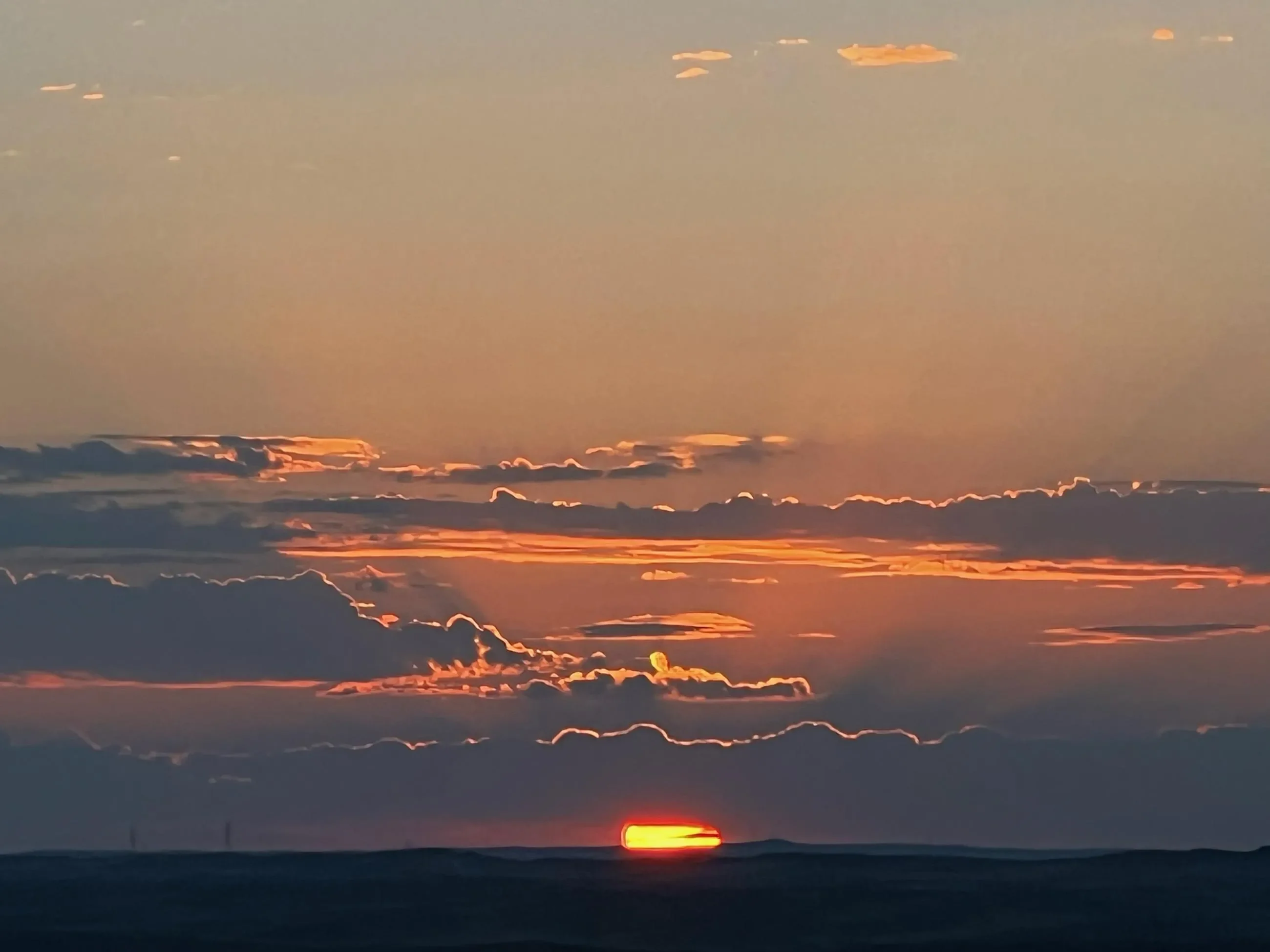 The sun just begins to rise over the horizon, tinging the sky and clouds with pink and orange hues